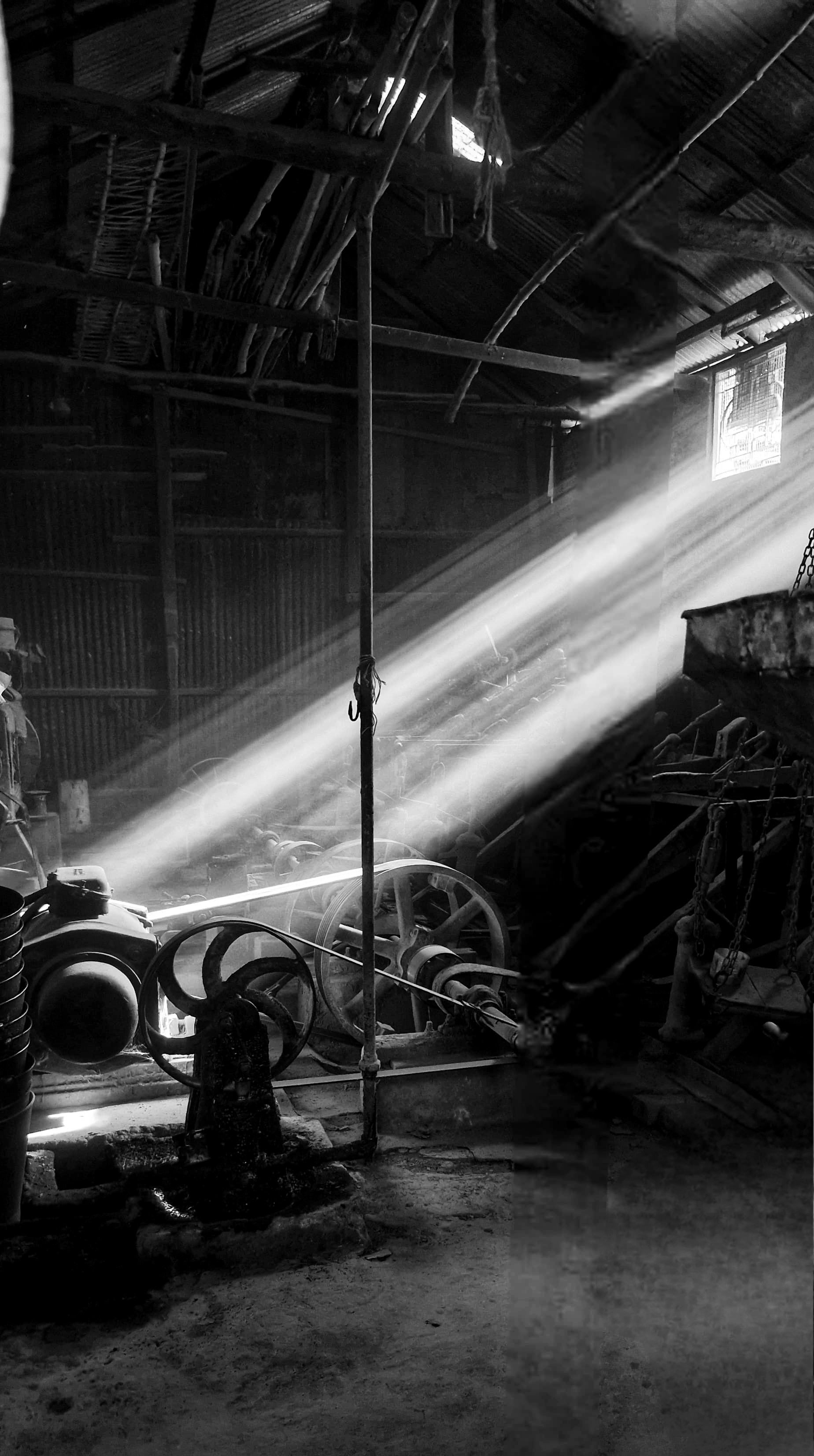 A black and white photo of a spinning wheel. Tools and equipment are visible all around.